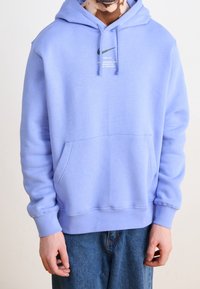 Light purple hoodie made from soft material, featuring a kangaroo pocket and a black Nike logo printed on the chest. Long sleeves with ribbed cuffs.