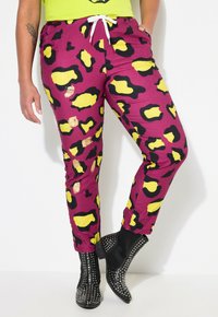Levendige paarse joggers met gele en zwarte luipaardprint, voorzien van een trekkoord in de taille en elastische boorden. Duidelijke versleten details.