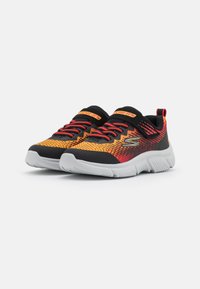Une paire de baskets pour enfants Skechers orange, rouge et noire avec des semelles blanches, des lacets rouges et des bandes Velcro sur un fond blanc.