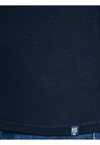 Top de tela acanalada azul marino con etiqueta "BIG STAR" cerca del dobladillo, combinado con vaqueros de mezclilla azul.