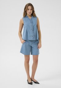 Denim ärmlös topp med volangkrage och knäppning fram, i kombination med knälånga randiga shorts. Ljust blå färgschema genom hela.