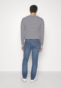 Striped long-sleeve shirt in navy and white, paired with blue jeans. The outfit features a casual fit and is complemented by white sneakers.