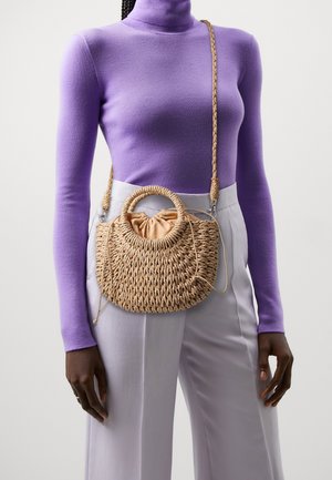 Flettet stråhåndtaske med rund top hank, naturlig farve, blødt stofindvendigt og justerbar flettet rem. Kombination med en lilla top.
