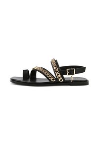 Mustat tasapohjaiset sandaalit, joissa on kaksi ristikkäin kulkevaa nyöriä, kultaketjusomiste ja säädettävä nilkkahihna neliösoljella.