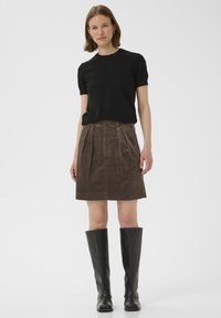 T-shirt noir à manches courtes associé à une jupe en velours côtelé marron avec des plis, portée avec des bottes en cuir noir jusqu'aux genoux. Texture lisse et design ajusté.