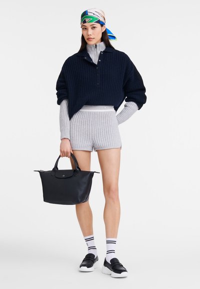 Navy ribbed oversized sweater, gray ribbed shorts, black leather handbag, black/platform loafers, and striped socks worn with a colorful scarf.