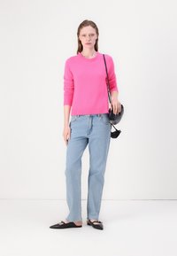 Lys rosa strikkegenser, lyseblå rette jeans, svarte flate sko og en liten svart crossbody-veske. Enkle og moderne kleskomponenter.