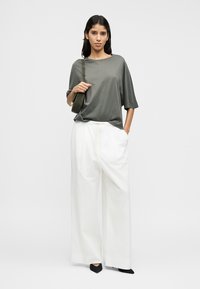 Γκρι κοντομάνικη μπλούζα σε συνδυασμό με άσπρο παντελόνι με φαρδιά μπατζάκια και μαύρα παπούτσια με μυτερή μύτη, μαζί με μια μικρή πράσινη τσάντα ώμου.