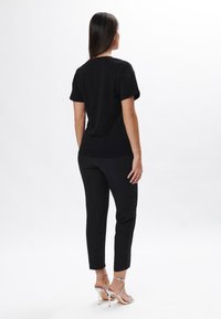 T-shirt nera a maniche corte abbinata a pantaloni neri aderenti, che mostrano una texture liscia e un design minimalista. Sandali con tacco alto argentati.