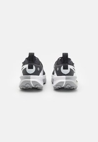 Scarpe da ginnastica in bianco e nero con una finitura testurizzata, dotate di una suola ammortizzata, linguette e un design del logo distintivo sul tallone.