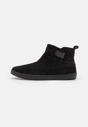 Botines de ante negro con textura suave, punta redondeada, suela baja de goma y una lengüeta en la parte trasera para facilitar su colocación.