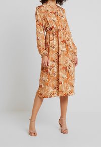 Robe midi à manches longues avec un motif floral aux nuances d'orange et de beige, dotée d'une taille élastique et d'un décolleté en V. Tissu lisse.