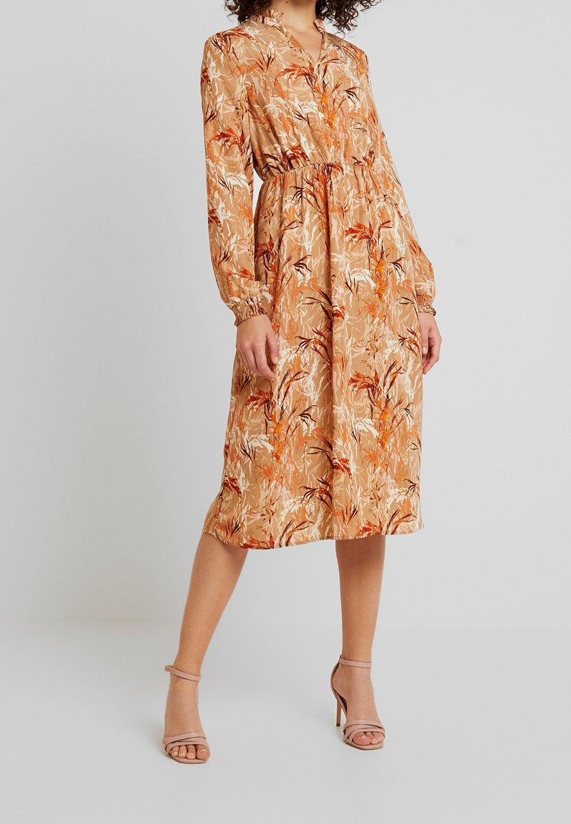 Robe midi à manches longues avec un motif floral aux nuances d'orange et de beige, dotée d'une taille élastique et d'un décolleté en V. Tissu lisse.
