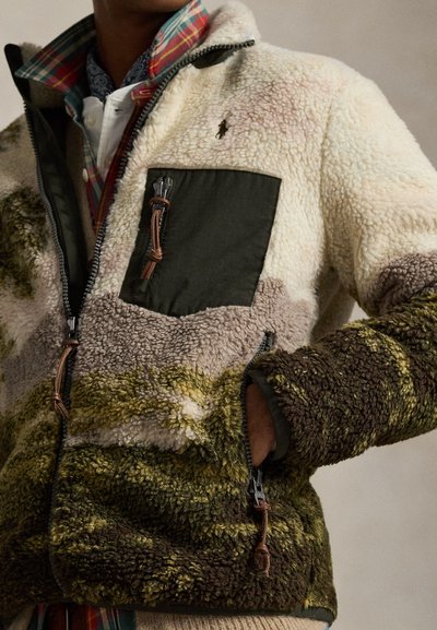 Gyapjúpulóver krémszín, olajbogyó és barna színek keverékével, zöld mellzsebbel, bőr részletekkel és cipzáras záródásokkal.