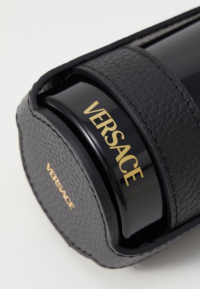 Porte-documents en cuir noir avec surface texturée, présentant un conteneur noir brillant avec "VERSACE" en lettres dorées, et un design élégant.