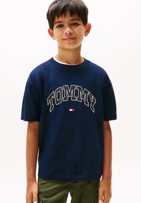 Tricou din bumbac bleumarin cu inscripția "TOMMY" în litere albe, având un mic accent de logo în roșu, alb și albastru aproape de talie. Mâneci scurte.