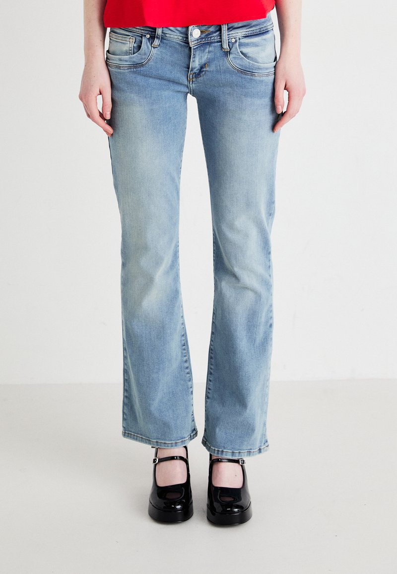 Light blue, flared denim jeans with faded areas and front pockets, paired with black platform shoes featuring ankle straps.