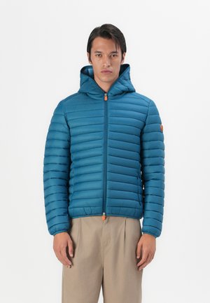 Teal puffer jacket with a hood, featuring horizontal quilted pattern, front zipper with orange pull, and a logo patch on the left sleeve.