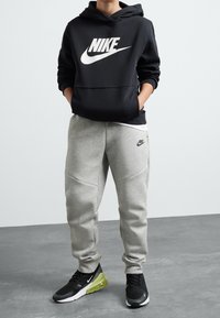 Černá mikina Nike s velkým bílým logem, v kombinaci s světle šedými tepláky s logem. Černé tenisky s zelenými akcenty.