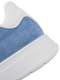 Nahaufnahme der Ferse eines blauen Wildleder-Sneakers mit weißem Lederbesatz und dicker weißer Gummisohle vor weißem Hintergrund.