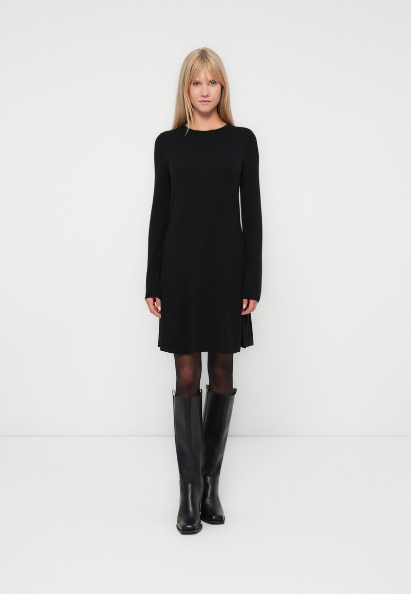 Robe noire à manches longues avec une coupe droite, texture douce, longueur genoux, associée à des bottes noires jusqu'aux genoux avec une finition lisse.