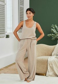 Beige tílko a široké kalhoty vyrobené z měkké, texturované tkaniny. Tento outfit se vyznačuje volným střihem a pružným pasem.