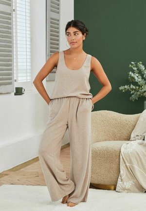 Top in beige e pantaloni a gamba larga realizzati in un morbido tessuto testurizzato. L'outfit presenta una vestibilità comoda e una cintura elastica.