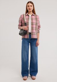 Camicia a quadri rosa e verde, abbinata a jeans a gamba larga blu chiaro e scarpe rosa. Borsa a tracolla nera con strap regolabile.