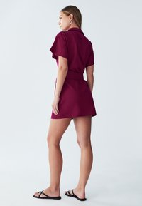 Lühike burgundi värvi kleit lühikeste varrukatega, krae ja vöökohtaga. Omab vabalt langevat lõiget ja minimalistlikku disaini. Kanda mustade sandaalidega.