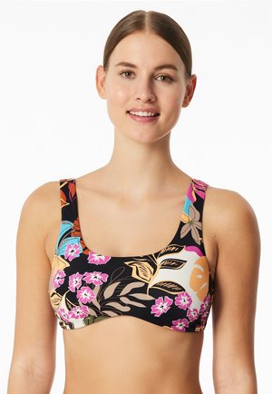 Junge Frau mit braunem zurückgebundenem Haar trägt ein Bikinioberteil mit Blumenmuster in Pink, Beige, Blau und Schwarz und lächelt leicht.