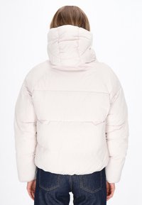 Flauschige, hellrosa Jacke mit hohem Kragen und horizontalen Nähten. Das Material wirkt glatt und leicht glänzend. Getragen mit dunkler Jeans.
