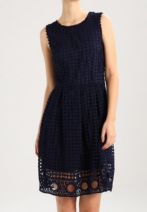 Ärmelloses, marineblaues knielanges Kleid mit strukturiertem geometrischem Muster und transparentem Saum mit kreisförmigen Ausschnitten.