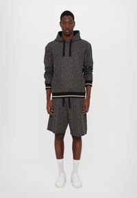 Sudadera con capucha negra con un patrón repetido, combinada con pantalones cortos negros a juego. Acentuada con zapatillas blancas y calcetas de caña corta.