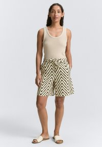 Un débardeur beige associé à un short taille haute avec un motif zigzag noir. Le short est doté d'une taille nouée et de deux poches latérales.