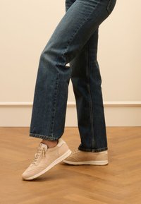 Sneaker beige con un mix di pelle liscia e morbida scamosciata. Le caratteristiche includono un design con lacci, cuciture sottili e una suola in gomma bianca.