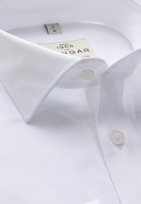 Valge krae shirt, millel on sile tekstuuriga kangas, kaks nuppu krae juures ja silt, mis näitab brändi ja suurust.