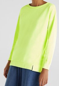Sudadera de manga larga en color amarillo neón, con un escote redondeado, aberturas laterales en el dobladillo y puños y cinturilla acanalados. Tejido suave, corte relajado.