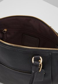 Borsa a mano in pelle nera con finitura testurizzata, zip dorata e fodera in tessuto marrone scuro. Presenta una tasca interna con zip e un'etichetta.