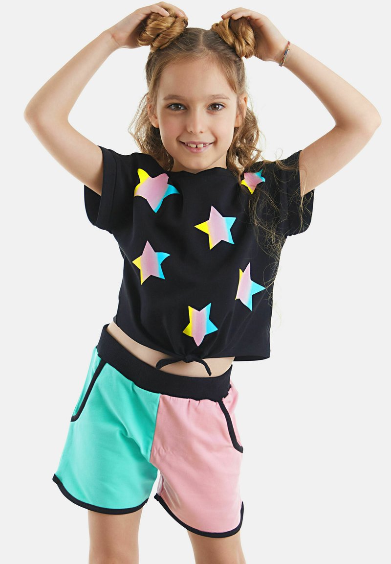 Schwarzes kurzes T-Shirt mit bunten Sterne-Applikationen. Mintgrüne und pinke Shorts mit einem schwarzen Bund und seitlichen Taschen.