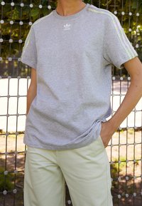 Grå t-shirt med kort ärm och Adidas-logotyp samt flerfärgade ränder på axlarna, ihop med ljusgröna byxor. Mjuk tygkvalitet.