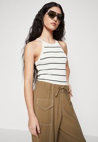 Hvitstripet tank topp med bølget kant, kombinert med løse brune bukser med lommer og kontraststing. Mørke solbriller.