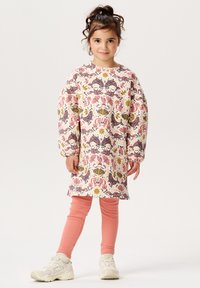Sukienka z długim rękawem w kolorowy print kwiatowy i paisley, wykonana z lekkiego materiału. Połączona z różowymi legginsami w prążki i białymi sneakerami.