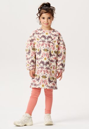 Sukienka z długim rękawem w kolorowy print kwiatowy i paisley, wykonana z lekkiego materiału. Połączona z różowymi legginsami w prążki i białymi sneakerami.