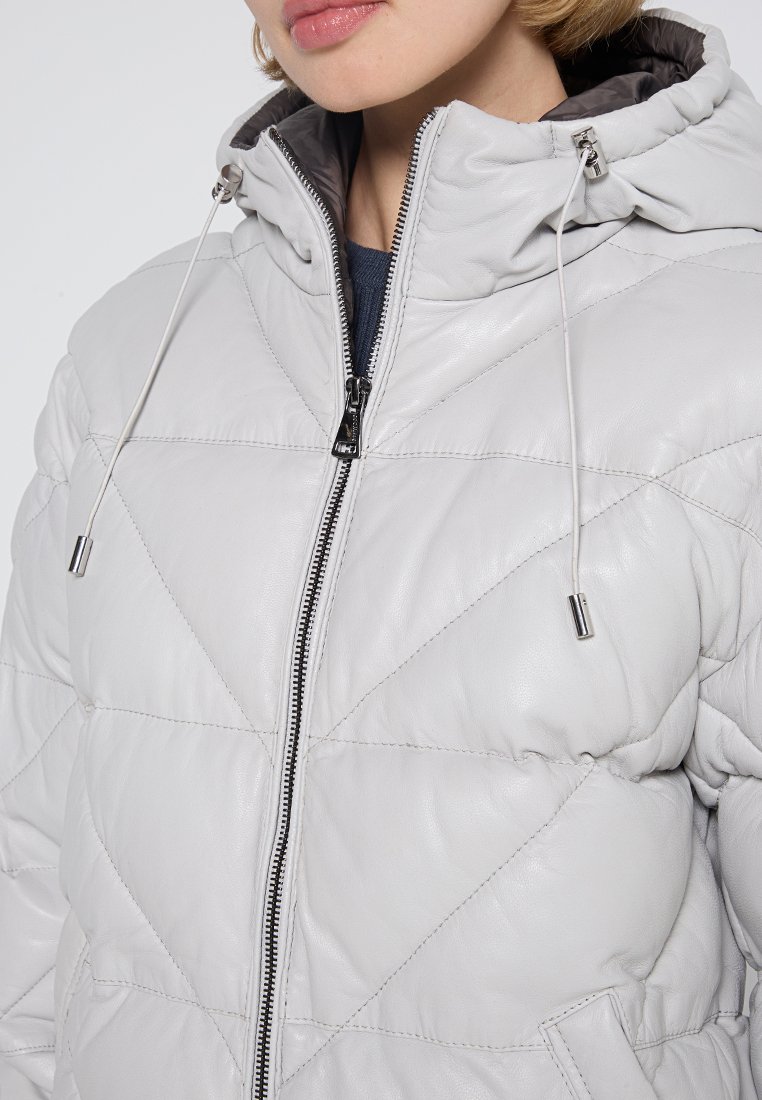 Chaqueta de cuero acolchada en gris claro con cierre de cremallera, capucha ajustable y herrajes plateados. Presenta costuras diagonales y bolsillos laterales.