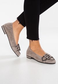 Ballerine in suede grigio con un fiocco decorativo impreziosito da perline nere tonde, tacco basso e texture liscia, abbinate a jeans neri con orlo sfilacciato.