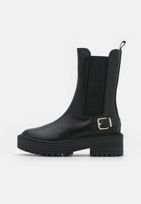 Botines negros con un exterior de cuero liso, paneles laterales elásticos, un acento de hebilla, suela gruesa y una suela de tracción texturizada.