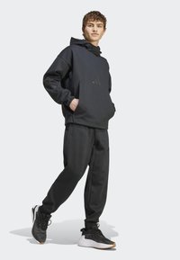 Black hoodie with a front pocket and logo detail, paired with matching tapered sweatpants and black athletic shoes with white accents.