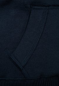 Marinblå sweatshirttyg med en synlig fickseam och ribbat nederkant. Mjuk textur med en jämn yta och robusta sömnadsdetaljer.