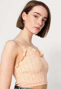 Top cropped laranja claro com decote com babados e alças finas, apresentando um design texturizado, franzido e um pequeno padrão xadrez.