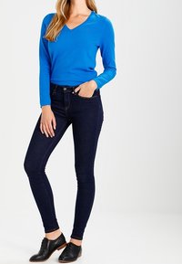 Niebieska bluzka z dekoltem w serek i długim rękawem zestawiona z ciemnoniebieskimi jeansami typu skinny oraz czarnymi butami na sznurowadła. Prosty design z dopasowanym krojem.